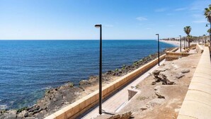 A coastal walkway with a clear view of the sea, a stone barrier, and a row of palm trees. - Roquetas Beachside Getaway (Roquetas del Mar)
