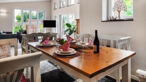 Een eetgedeelte met een houten tafel voor vier personen, omringd door witte stoelen.
