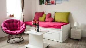 Une chambre à coucher avec un lit, une table de chevet blanche, une table blanche, une chaise rose et une fenêtre avec des rideaux.