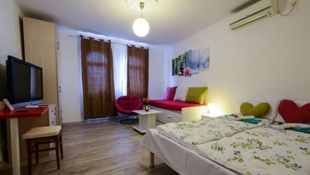 Une chambre à coucher avec un lit, un bureau avec une télévision, une chaise et une fenêtre avec des rideaux.