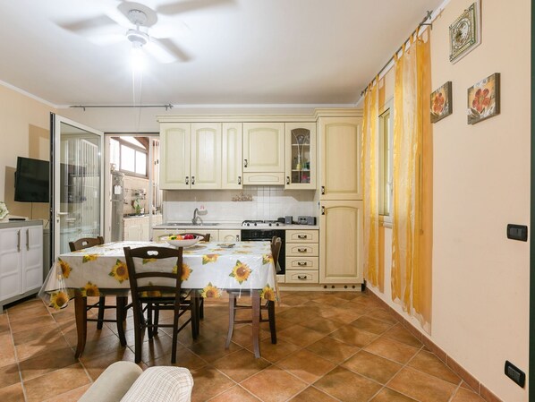 A compact kitchen with white cabinets, a dining table with chairs, and a ceiling fan.