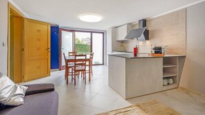 A modern kitchen with a built-in island, a dining area with wooden chairs, and a sliding glass door leading to a balcony. - Cottage in Aywaille with Garden (Aywaille)