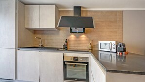 A modern kitchen with built-in appliances, a microwave, and a wine bottle on the counter. - Cottage in Aywaille with Garden (Aywaille)