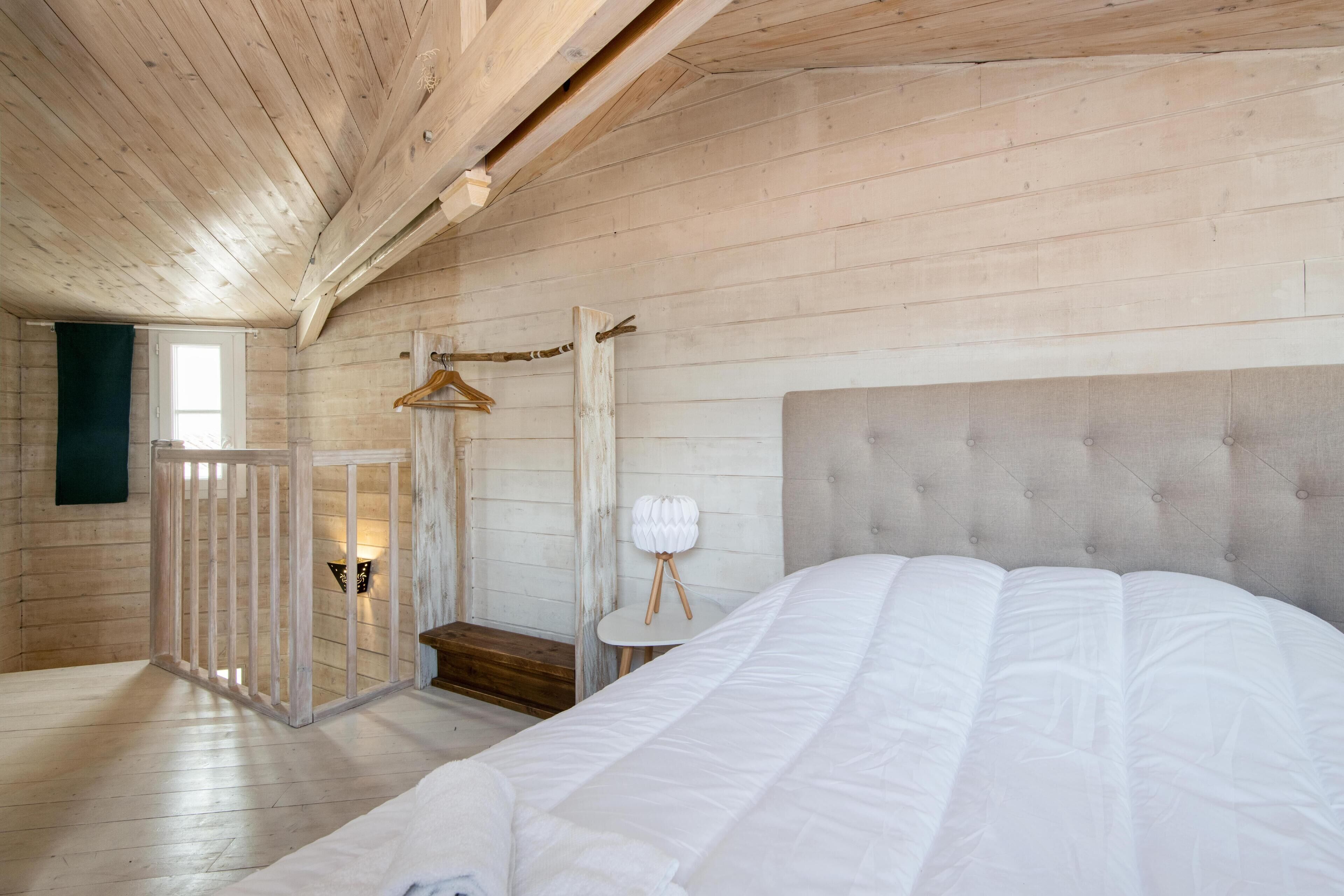 A bedroom with a large bed, wooden walls, a hanging light fixture, and a small table with a lamp.