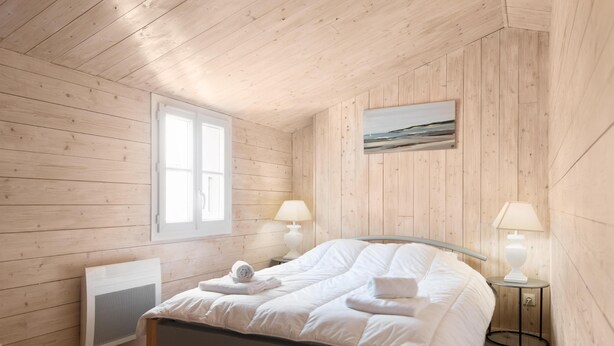 A wooden-paneled bedroom with a bed, two bedside lamps, a window, and a painting on the wall. - ELOISE             . (Sainte-Marie-de-Ré)