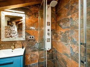 Relax in a bathroom with a glass shower enclosure, white sink, and blue vanity cabinet, surrounded by textured tiles and a decorative mirror.