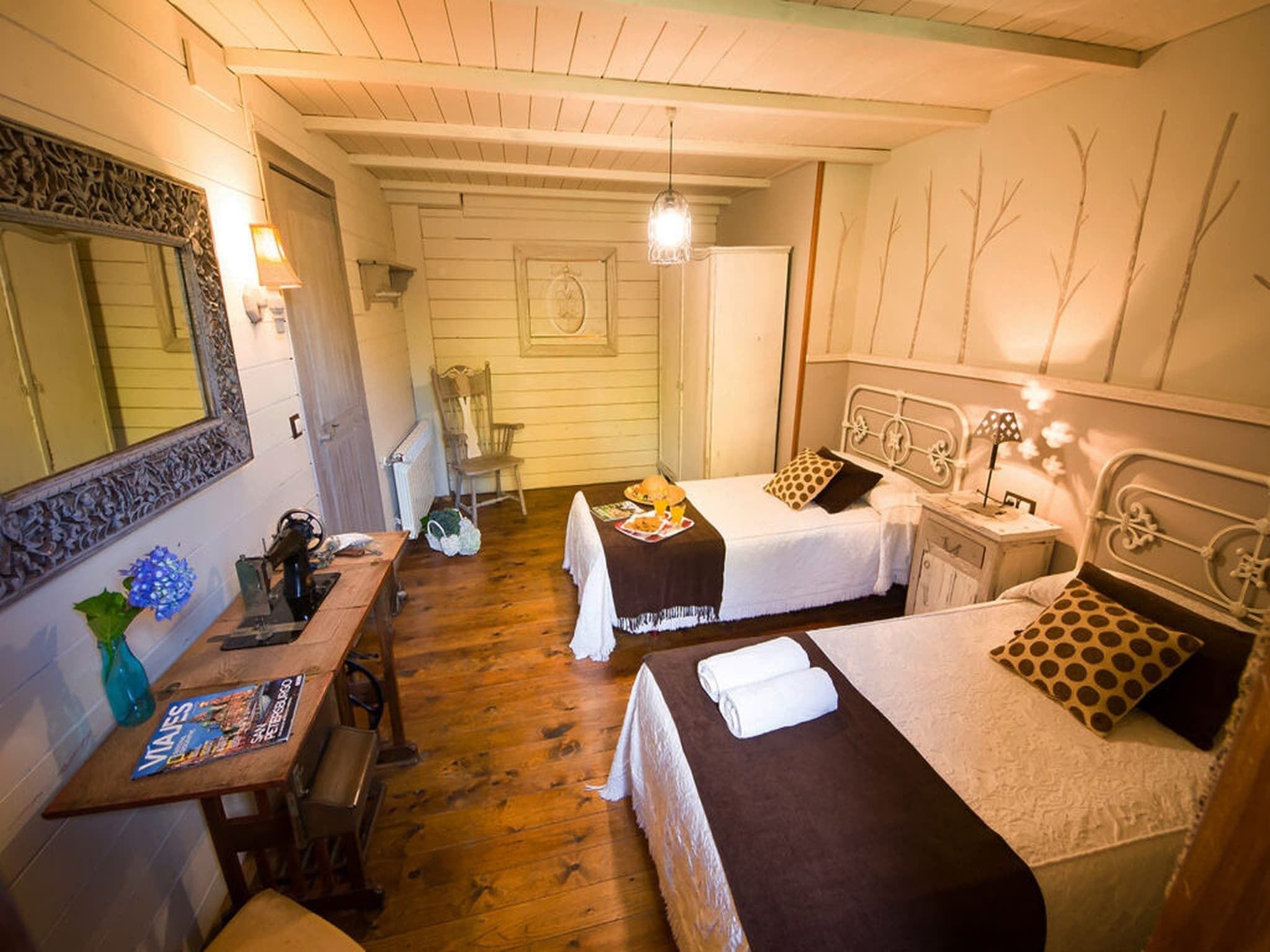 A cozy room with two beds, a wooden desk, a mirror, and a hanging light fixture.
