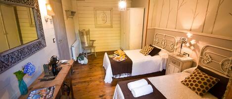A cozy room with two beds, a wooden desk, a mirror, and a hanging light fixture.