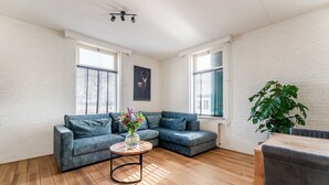 A modern living room with a sectional sofa, a round coffee table with flowers, and a large plant. - Farmhouse in Silvolde with Hot Tub (Silvolde)