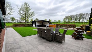 A patio with a dining table and chairs, a small building, and a well-maintained lawn. - Farmhouse in Silvolde with Hot Tub (Silvolde)