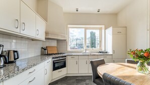 A modern kitchen with white cabinetry, a granite countertop, a built-in oven, and a dining area with a wooden table and chairs. - Farmhouse in Silvolde with Hot Tub (Silvolde)