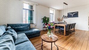 A modern living room with a sectional sofa, a dining table with chairs, and a vase of flowers on a round table. - Farmhouse in Silvolde with Hot Tub (Silvolde)
