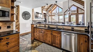 A modern kitchen with wooden cabinetry, a built-in microwave, and a large window providing natural light. - Bachelor Gulch Village (Avon)
