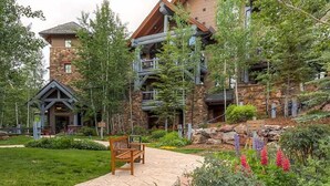 A lodge with stone and wood architecture, a stone pathway, and a bench. - Bachelor Gulch Village (Avon)