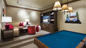 A cozy living room with a pool table, a sofa, and a television.