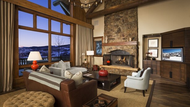 A cozy living room with a fireplace, comfortable seating, and a large window overlooking a snowy landscape.