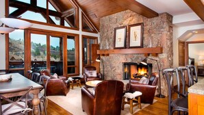 A spacious living area with a stone fireplace, leather furniture, and large windows offering a view of the outdoors.