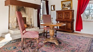 A room with a fireplace, a wooden cabinet, a table with a candle, and patterned chairs.