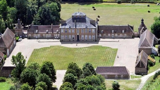 A large, historic building with a symmetrical facade, a central courtyard, and surrounding trees.