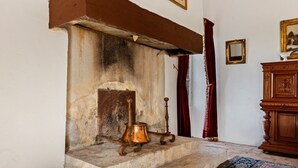 A stone fireplace with a copper pot and a wooden stand, a red curtain, and a patterned rug on a tiled floor.