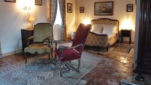 A traditional room with a bed, two chairs, a rug, and a wooden ceiling.