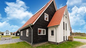 Et moderne hus med en sort og hvid facade, rødt tag og en belagt indkørsel.