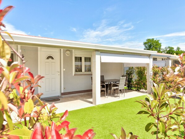 A single-story house with a covered patio area, a front door, and a small garden with artificial grass.