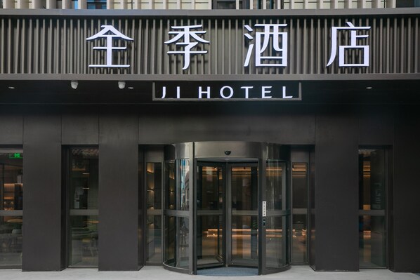 Entrada de un hotel con puerta giratoria y un cartel que dice 'JI HOTEL'.