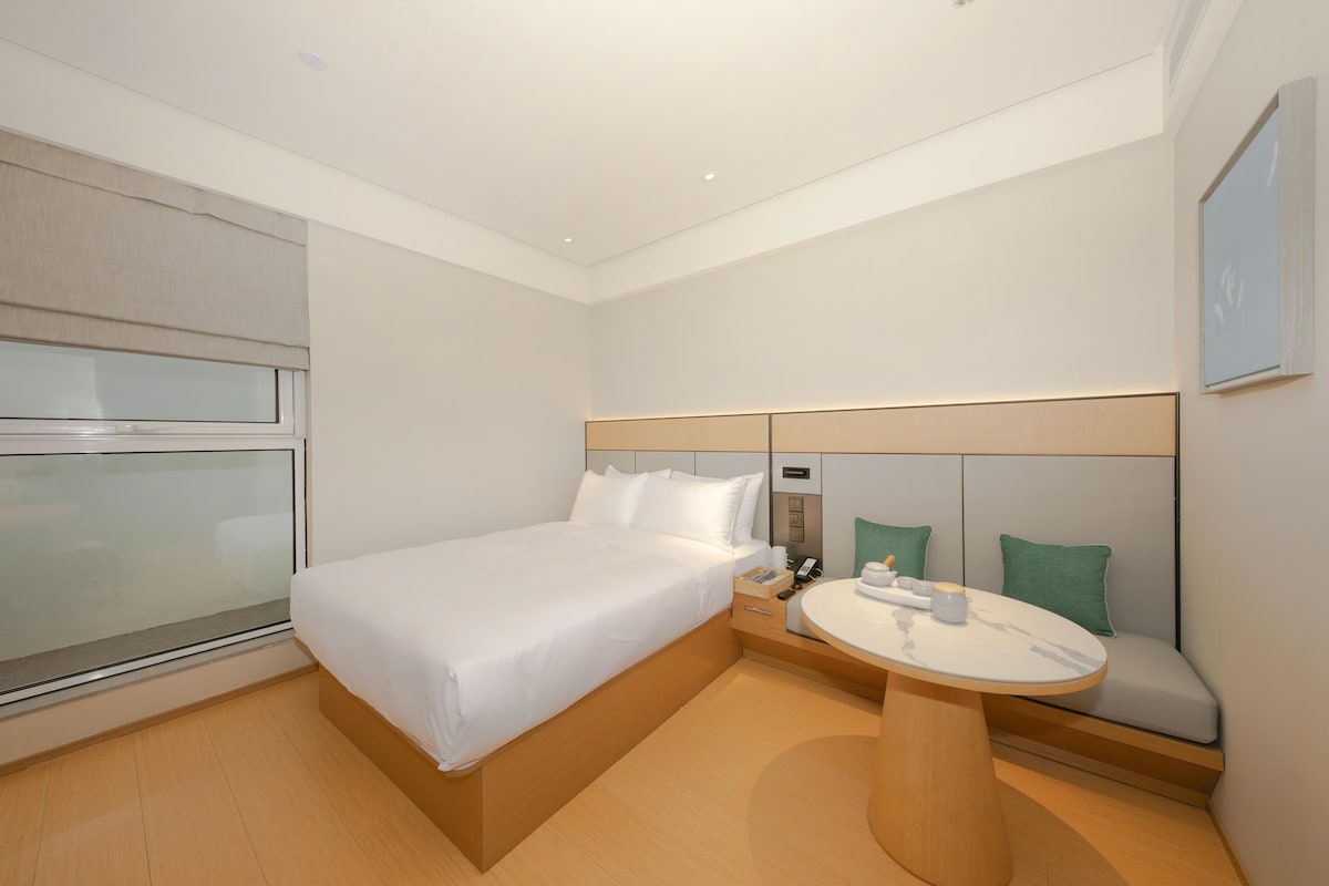 A hotel room with a bed, bedside table, and a small seating area with a table.