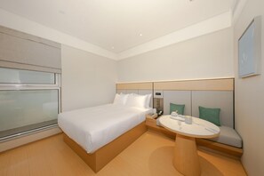 Et hotelværelse med en seng, et natbord og et lille siddeområde med et bord.