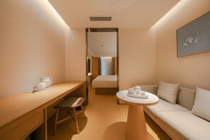 Habitación de hotel compacta con cama, sofá, una mesita y un escritorio con silla.