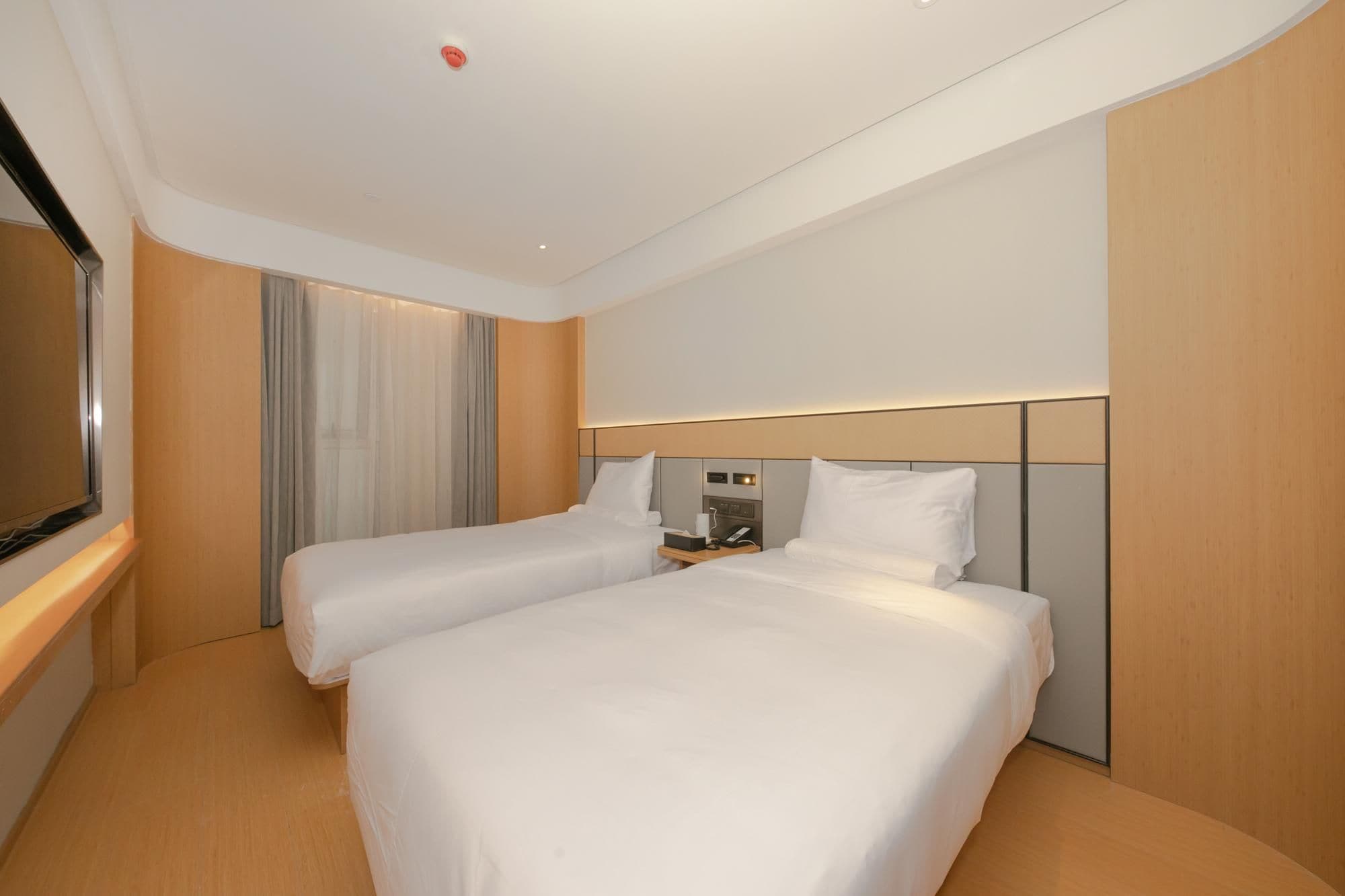 A hotel room with two beds, a TV, and a bedside table with a lamp.