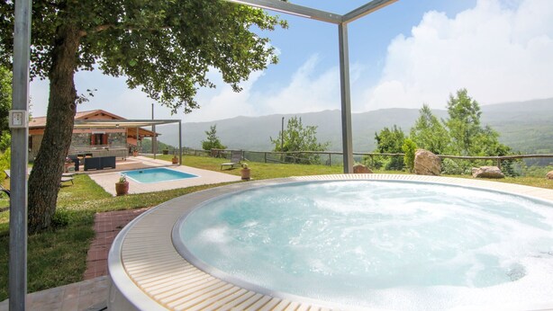 Hidromassatge amb vista a les muntanyes, una piscina i zona de terrassa amb mobles d'exterior.