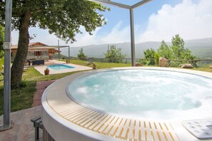 Een hottub met uitzicht op bergen, een zwembad en een terras met tuinmeubilair.