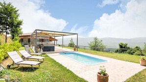 Zona de piscina amb gandules, una pèrgola i vista a les muntanyes.