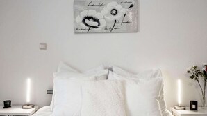 A neatly made bed with white bedding and multiple pillows, a wall-mounted artwork of flowers, and bedside tables with candles and small vases. - Charming gite in Waimes near Spa-Francorchamps (Waimes)