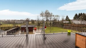 A wooden deck with a metal railing, a small shed, and a green field in the background. - Charming gite in Waimes near Spa-Francorchamps (Waimes)