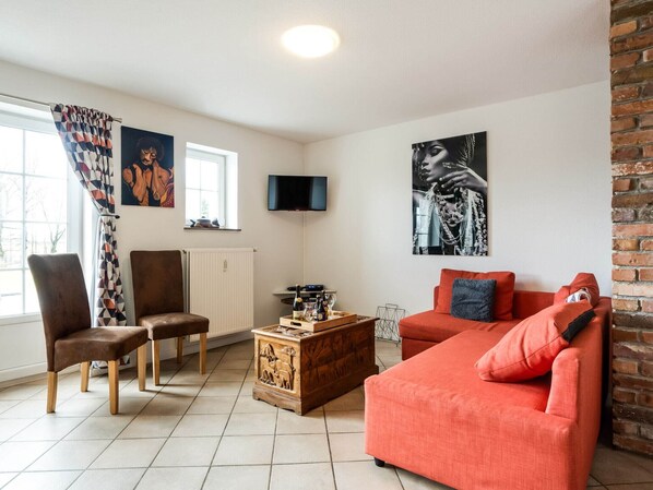 A living room with a red sofa, a brown chair, a wooden coffee table, and a television mounted on the wall. - Charming gite in Waimes near Spa-Francorchamps (Waimes)