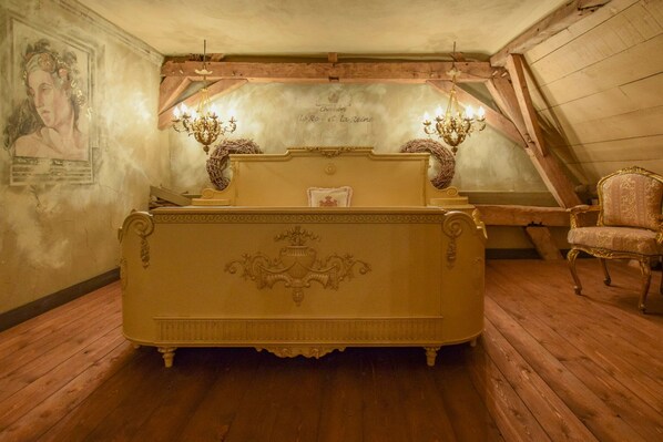 A bedroom with a large ornate bed, a chandelier, and a chair.