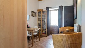 Ein gemütliches Zimmer mit Holzboden, einem Esstisch mit Stühlen, einem Korbstuhl, einem Bücherregal und einer Heizung.
