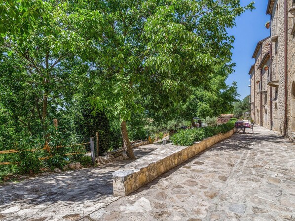 Eine von Bäumen gesäumte Kopfsteinpflasterstraße, vorbei an einem Steinhaus mit Rundbogenfenstern.