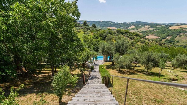 Eine steile Steintreppe führt bergauf, im Hintergrund ist ein Pool und Bäume zu sehen.