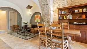 A rustic dining area with a stone wall, wooden furniture, and a bookshelf filled with books and kitchenware.