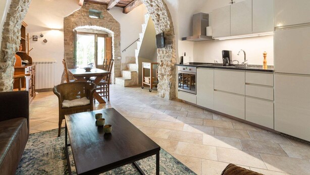 A rustic kitchen with stone walls, a wooden dining table, and a modern oven.