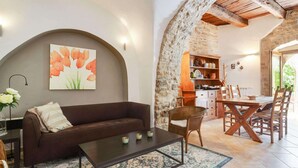 A cozy living area with a brown sofa, a coffee table, and a painting of flowers. There is a stone wall and a wooden table with chairs.