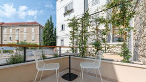 A balcony with two white chairs and a small table, overlooking a cityscape with buildings and a clear sky. - Stonemasons Heritage (Split)