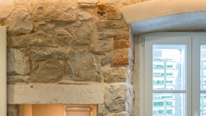 A stone fireplace with a vase of flowers, a window with white shutters, and a brick wall. - Stonemasons Heritage (Split)