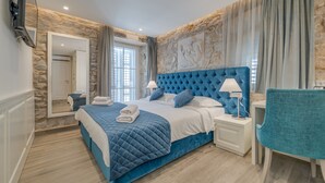 A bedroom with a stone wall, a large bed with a blue headboard, a bedside table with a lamp, and a chair. - Stonemasons Heritage (Split)