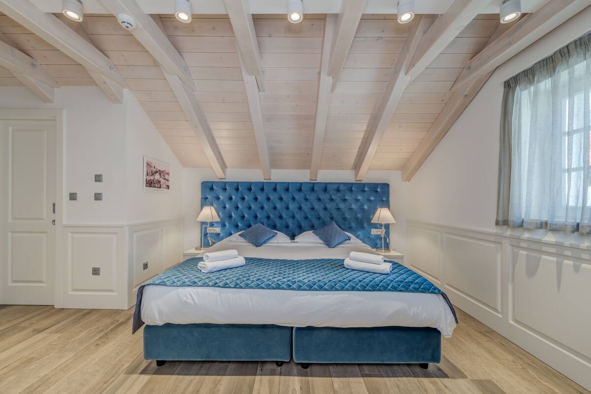 Un dormitorio con una cama grande, vigas de madera en el techo y una ventana con cortinas.