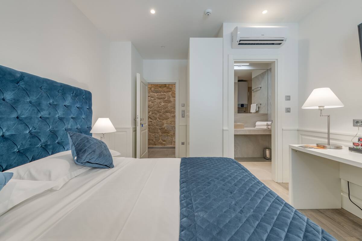 Un dormitorio moderno con una cama grande, dos lámparas de noche, un escritorio y un baño visible a través de una puerta abierta.